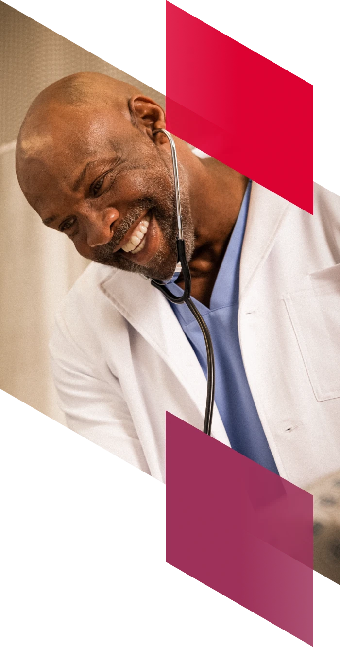 A locums physician smiles while listening to his stethoscope at work